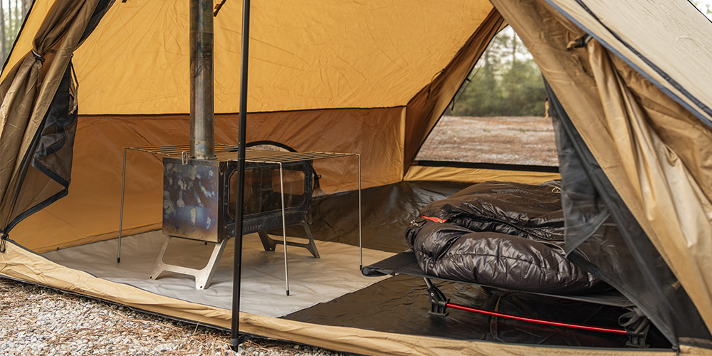 Hot tenting setup in New Zealand's snowy wilderness, showcasing a tent with a wood stove in a winter landscape.